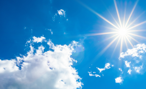 Blue sky with bright sun and some fluffy white clouds