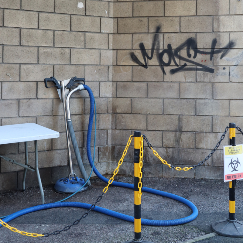 Image of cleaning equipment next to a wall marked with graffiti tagging